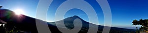 Beautiful landscape of volcano mountain during sunny day morning with forest in foregound and blue sky in background