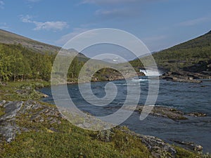 Beautiful landscape with waterfall on wild Tjaktjajakka river, birch tree forest and mountains. Lapland naturein summer at