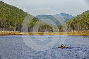 A fisherman on a rubber boat with oars floats on a calm lake amid green hills