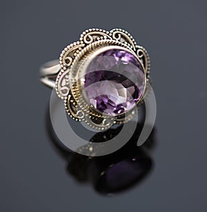 Beautiful large purple shining gemstone ring photo with gold colored band on a black shiny surface