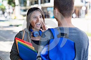Beautiful latin american female student talking with male student in city