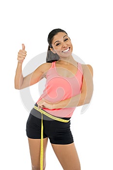 Beautiful latin woman in fitness clothes measuring body waist size holding measure tape smiling happy