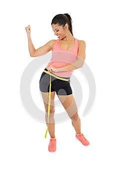 Beautiful latin woman in fitness clothes measuring body waist size holding measure tape smiling happy