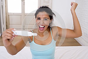 Beautiful latin woman holding pregnancy test looking and finding positive result smiling happy and excited