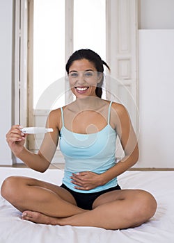 Beautiful latin woman holding pregnancy test looking and finding positive result smiling happy and excited