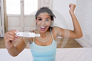 Beautiful latin woman holding pregnancy test looking and finding positive result smiling happy and excited