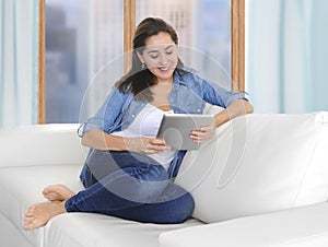 Beautiful Latin woman sitting on living room sofa couch at home enjoying using digital tablet computer