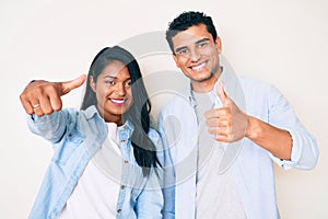 Beautiful latin young couple wearing casual clothes approving doing positive gesture with hand, thumbs up smiling and happy for