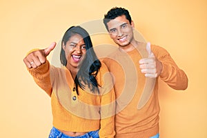 Beautiful latin young couple wearing casual clothes together approving doing positive gesture with hand, thumbs up smiling and