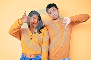 Beautiful latin young couple wearing casual clothes together doing thumbs up and down, disagreement and agreement expression