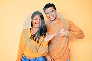 Beautiful latin young couple wearing casual clothes together showing palm hand and doing ok gesture with thumbs up, smiling happy