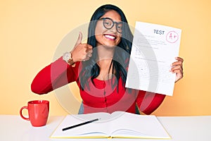 Beautiful latin young woman with long hair showing a passed exam smiling happy and positive, thumb up doing excellent and approval