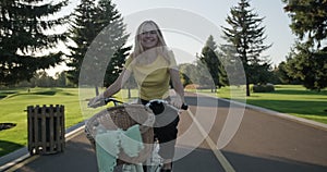 Beautiful laughing happy girl teenager rides bicycle in park, girl rides on camera