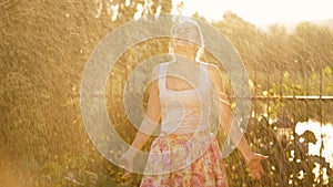 Beautiful laughing woman having fun under sparkling water from garden hosepipe at sunset