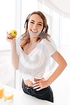 Beautiful laughing young lady with headphones eating apple.