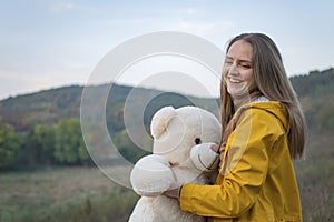 Beautiful laughing young woman with teddy bear on autumn day. Happy young woman in yellow parka jacket walks in nature