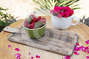 Beautiful layout with board with bowl with strawberries lying on table with cup with roses.