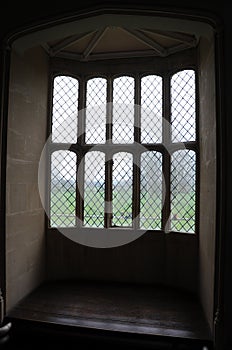 Beautiful leaded window in old building with sunlight entering. Green grass countryside view from the window.