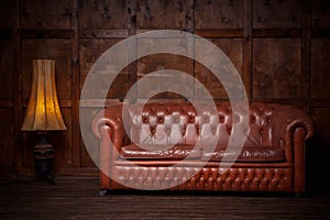 Beautiful leather sofa chester brown. In the interior of the loft of dark color, with a wooden wall in the background