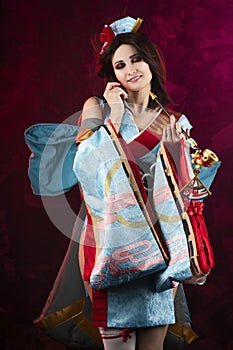 Beautiful leggy busty cosplayer girl wearing a stylized Japanese kimono costume cheerfully posing holding a fake pipe on a blue