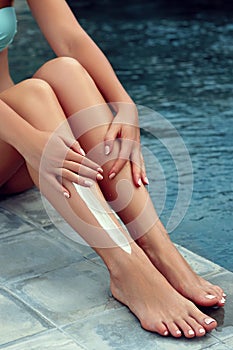 Beautiful legs outdoors by pool under sunshine on summer day. Woman apply sun protection cream on her smooth tanned legs. Skincare