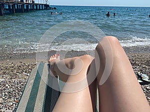 Beautiful legs of a woman with a pedicure having a rest on a sun lounger on the beach by the sea