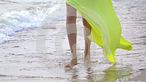 Beautiful legs of young girl wearing long yellow dress running barefoot sand on sea beach close up wind breeze waves