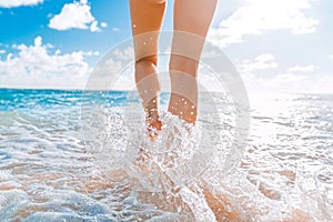 Beautiful legs of a young girl who runs towards the ocean on a sandy beach. The wave breaks against the girl`s legs. Ghostly ocea