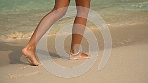 Beautiful legs of a young girl wolking on the beach