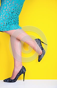 Beautiful legs of young woman in colorful skirt and black shoes with high heels on vibrant yellow background