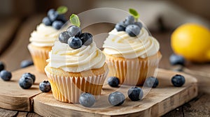 Beautiful lemon vanilla cupcakes with cream cheese frosting decorated with fresh blueberries and green leaves. Close up food