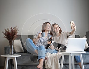 Beautiful lesbian family with dog sitting oh gray sofa at home and spending time together taking selfie on smartphone