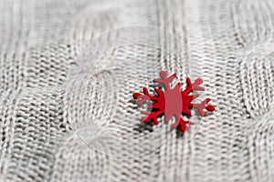 Beautiful light gray knitted pattern with red paper snowflake , knitted scarf close up. Knitted background.