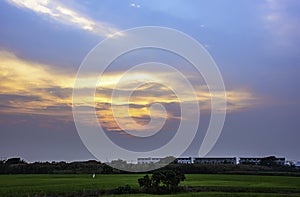 Beautiful light of Sunset with clouds in the sky reflection behind the building and paddy fields