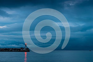 Beautiful lighthouse on the seashore at dusk, rainy clouds over