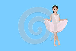 Beautiful little Asian child girl in pink tutu skirt dancing over blue background with copy space. Children is studying ballet