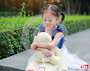 Beautiful little Asian girl dressed with a fantasy outfit sitting in the garden with teddy bear