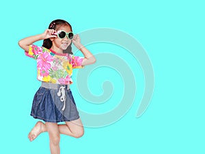 Beautiful little Asian kid girl wearing a flowers summer dress and sunglasses  on cyan background with copy space. Summer