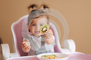 Beautiful little baby girl first time eating exotic fruits in high chair. Cute baby girl taste delitious fruist, mango