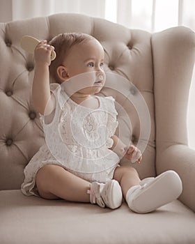 Beautiful little baby girl sitting on the chair and holding hair comb