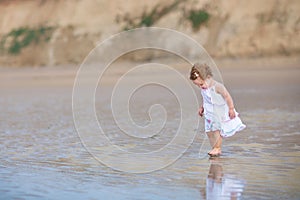 Beautiful little baby girl wearing white dress on beach