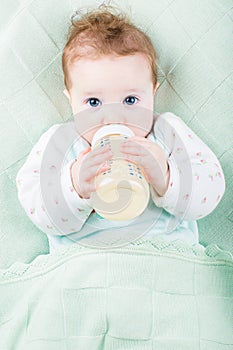 Beautiful little baby with a milk bottle under knitted blanket