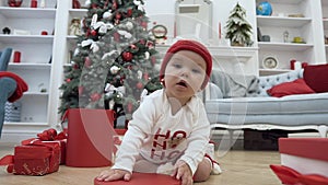 Beautiful little baby playing with red lid of the christmas box sitting on the wooden floor in the middle of the the