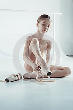 Beautiful little ballerina in blue dress for dancing puting on foot pointe shoes