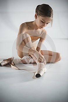 Beautiful little ballerina puting on foot pointe shoes