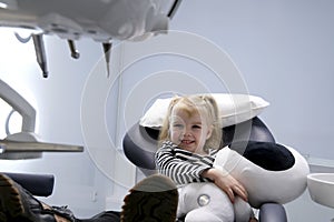 beautiful little blond blonde girl in dentist office big shoes on feet close-up latest technology soft toy in hands