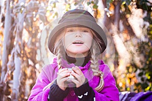 Beautiful little blond girl in a hat drinking coffee or tea in the autumn park. child drink tea in the park