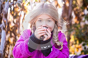 Beautiful little blond girl in a hat drinking coffee or tea in the autumn park. child drink tea in the park