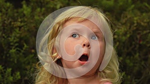 Beautiful little blond girl is looking up in the sky in amazement
