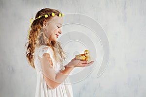Beautiful little blonde girl in floral wreath holds yellow duck in her hands. Easter concept. Easter card. Copy space for your